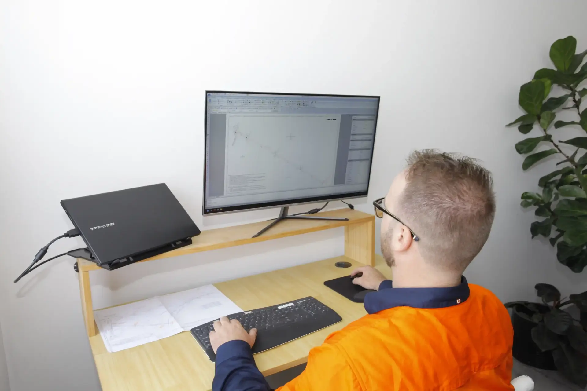Registered land surveyor drafting cadastral plan in BricsCAD at office desk with survey field notes, Sydney NSW